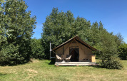 Tienda safari Tente Canadienne en Huttopia Les Falaises, Normandía, rodeada de árboles y césped verde.