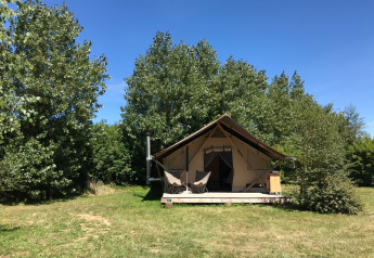 Tienda safari Tente Canadienne en Huttopia Les Falaises, Normandía, rodeada de árboles y césped verde.