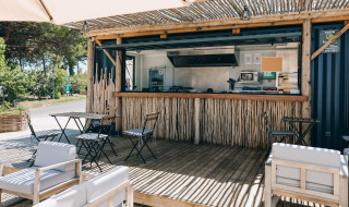 Cafetería al aire libre con mobiliario de madera y barra de bambú en Camping Seasonova Ile de Ré en Nouvelle-Aquitaine, Francia.
