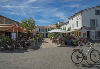 Udendørs caféer og cykler på en solrig dag i en charmerende landsby ved Camping Seasonova Ile de Ré, Frankrig.