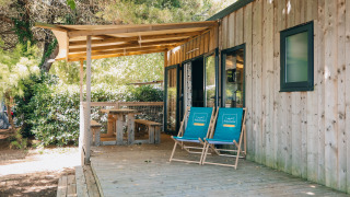 Acogedora cabaña Cottage Prestique con terraza de madera, dos sillas azules y área de picnic techada.