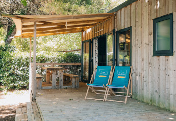 Charmant Cottage Prestique avec terrasse en bois, deux chaises bleues et coin repas extérieur couvert.