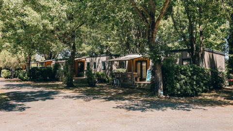 Cottage Prestige op Camping Seasonova Ile de Ré, Frankrijk, genesteld tussen groene bomen en struiken.