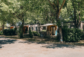 Cottage Prestige op Camping Seasonova Ile de Ré, Frankrijk, genesteld tussen groene bomen en struiken.