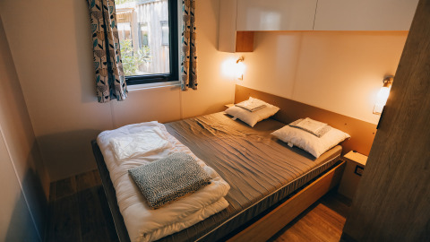 Sfeervolle slaapkamer in Cottage Prestique op Camping Seasonova Ile de Ré, Frankrijk, met groot raam en bed.