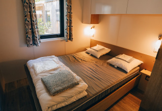 Sfeervolle slaapkamer in Cottage Prestique op Camping Seasonova Ile de Ré, Frankrijk, met groot raam en bed.