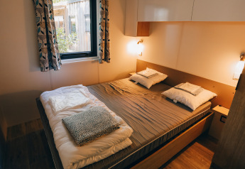 Et hyggeligt soveværelse i Cottage Prestique på Camping Seasonova Ile de Ré med dobbeltseng og vindue.