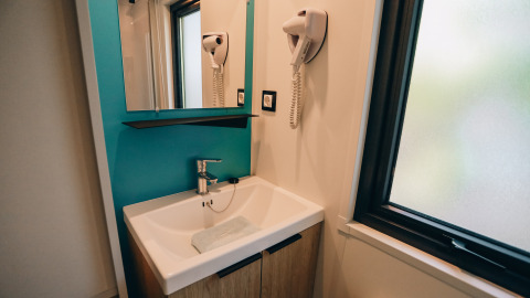 Moderne wastafel met spiegel, haardroger en raam in Cottage Prestique op Camping Seasonova Ile de Ré, Frankrijk.