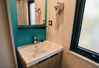 Moderne wastafel met spiegel, haardroger en raam in Cottage Prestique op Camping Seasonova Ile de Ré, Frankrijk.