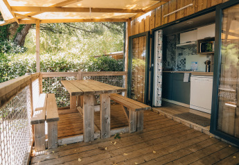 Udendørs træterrasse med bænk og bord, delvist overdækket, ved Cottage Prestique på Camping Seasonova Ile de Ré, Frankrig.