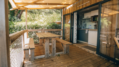 Udendørs træterrasse med bænk og bord, delvist overdækket, ved Cottage Prestique på Camping Seasonova Ile de Ré, Frankrig.
