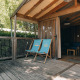 Udendørs terrasse med to liggestole i træhytte Lodge Premium omgivet af grønne træer og buske.