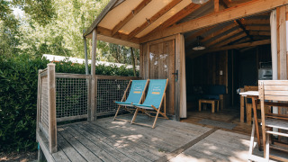 Porche de madera con dos tumbonas frente a la cabaña Lodge Premium, rodeado de vegetación verde.
