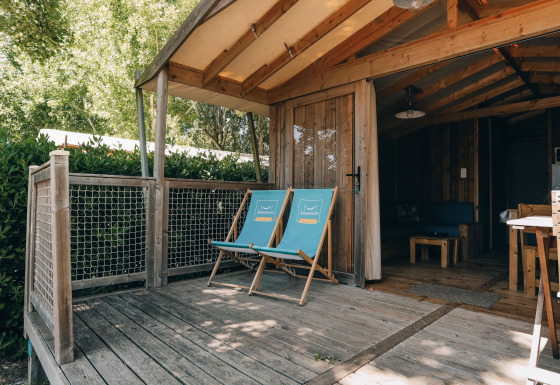 Holzterrasse mit zwei Liegestühlen vor der Lodge Premium Hütte, umgeben von viel Grün und Bäumen.