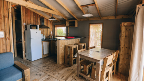 Binnenzicht van Lodge Premium bij Camping Seasonova Ile de Ré met houten meubilair en keukenhoek.