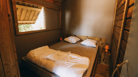 Sfeervolle houten slaapkamer van Lodge Premium aan Camping Seasonova Ile de Ré in Frankrijk, open raam.