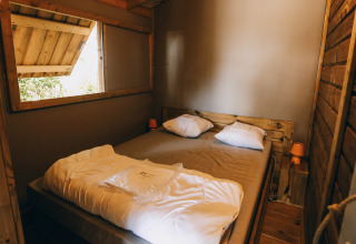 Sfeervolle houten slaapkamer van Lodge Premium aan Camping Seasonova Ile de Ré in Frankrijk, open raam.