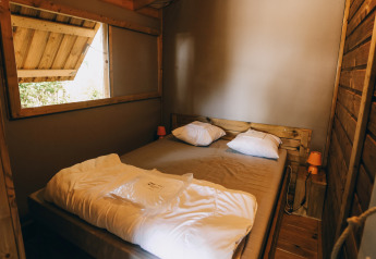 Accogliente camera da letto in legno Lodge Premium al Camping Seasonova Ile de Ré, Francia, con finestra aperta.