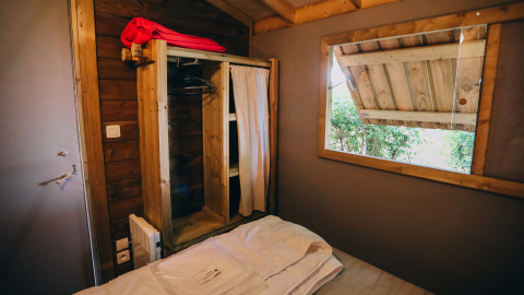 Slaapkamer in Lodge Premium bij Camping Seasonova Ile de Ré, met open raam en rustieke houten kast.
