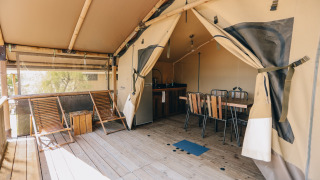 Safari tent at Slow Lodge with wooden deck, lounge chairs, dining table, and visible kitchen inside.