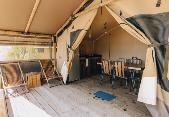 Tenda safari al Slow Lodge con terrazza in legno, sedie a sdraio, tavolo da pranzo e cucina visibile.
