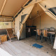Safari telt ved Slow Lodge med trædæk, loungestole, spisebord og synlig køkkenfacilitet indendørs.