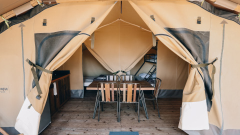 Safaritent Slow Lodge op Camping Seasonova Ile de Ré in Frankrijk met tafel, stoelen en bedden binnenin.