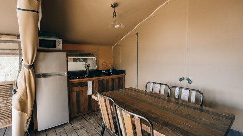 Interior view of a safari tent kitchen and dining table at Slow Lodge, Camping Seasonova Ile de Ré, France.