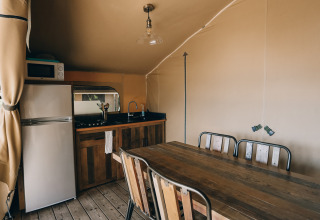 Interior view of a safari tent kitchen and dining table at Slow Lodge, Camping Seasonova Ile de Ré, France.