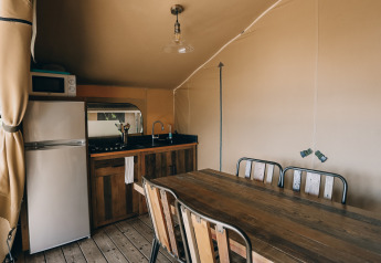Interior view of a safari tent kitchen and dining table at Slow Lodge, Camping Seasonova Ile de Ré, France.
