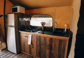 Zona de cocina en una tienda safari de Slow Lodge, Camping Seasonova Ile de Ré, con nevera y fogones.