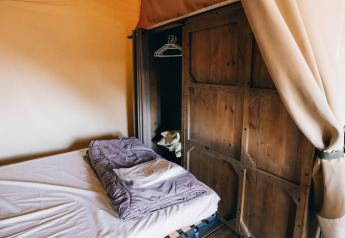 Interior de tienda safari en Slow Lodge, Camping Seasonova Ile de Ré, Francia, con cama y armario de madera.