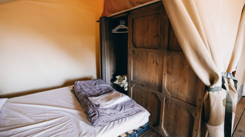 Interior de tienda safari en Slow Lodge, Camping Seasonova Ile de Ré, Francia, con cama y armario de madera.