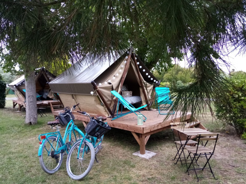 Twee tenten op houten platforms met fietsen, tuinstoelen en ligstoelen bij een gezellige camping.