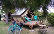 Twee tenten op houten vlonders met fietsen, tuinstoelen en ligstoelen tussen de bomen op de camping.