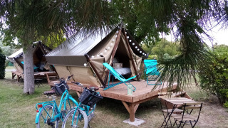 Zwei Zelte auf Holzterrasse mit Fahrrädern, Gartenmöbeln und Liegestühlen in einem grünen Campingplatz.