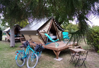 Zwei Zelte auf Holzterrasse mit Fahrrädern, Gartenmöbeln und Liegestühlen in einem grünen Campingplatz.
