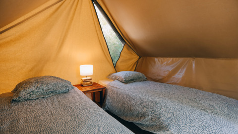 Twee eenpersoonsbedden met beddengoed en een nachtkastje met lamp in een gezellige tipi-tent.