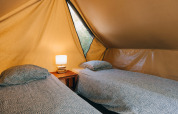 Two single beds with bedding and a bedside table with a lamp inside a cozy teepee tent interior.