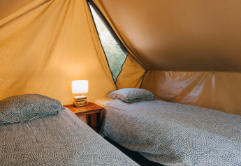 Two single beds with bedding and a bedside table with a lamp inside a cozy teepee tent interior.