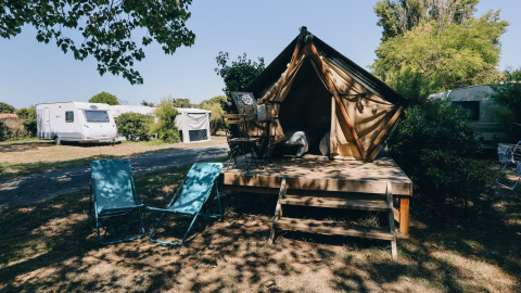 Cozy teepee tent campsite with outdoor chairs and caravans in the background on a sunny day.