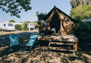 Campement douillet avec une tente tipi, chaises extérieures et caravanes en arrière-plan, au soleil.