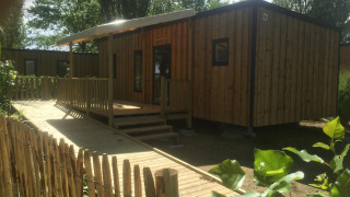 Accessible mobile home cabin with wooden ramp and terrace, suitable for disabled guests in a green setting.