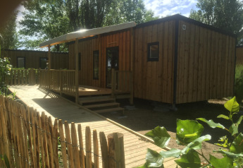 Barrierefreies Mobilheim mit Rampe und Terrasse, umgeben von Bäumen und Natur für Rollstuhlfahrer.