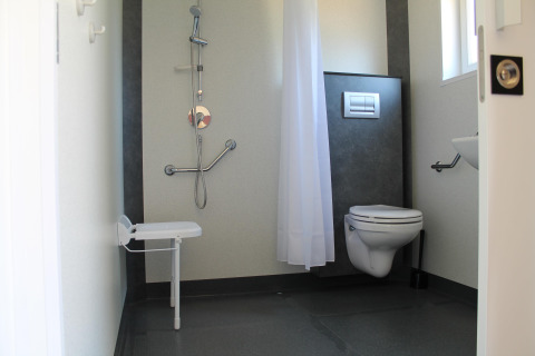Salle de bain accessible avec douche, siège rabattable, toilettes et barres d’appui en mobil-home en France.