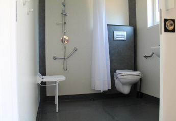 Accessible bathroom with shower, folding seat, toilet, and grab bars in a mobile home in France.