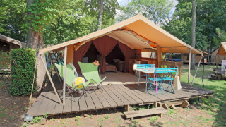 Tenda safari Bungalow Classic con veranda in legno, sedie e tavolo su un campeggio circondato dal verde.
