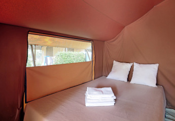 Interior de una tienda safari Bungalow tent Classic con cama doble, dos almohadas y una ventana lateral.