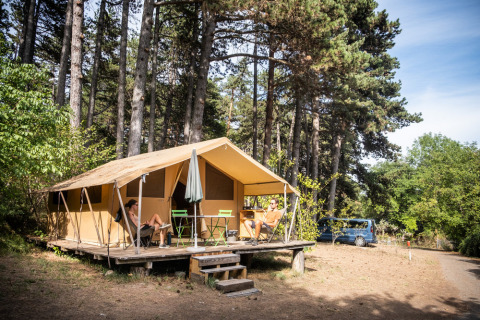 Twee mensen relaxen voor een Bungalow tent Classic safaritent op een bosrijke camping met een auto in de buurt.