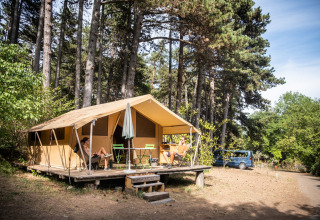 Two people relaxing in front of a Bungalow tent Classic safari tent at a wooded campsite with a car nearby.